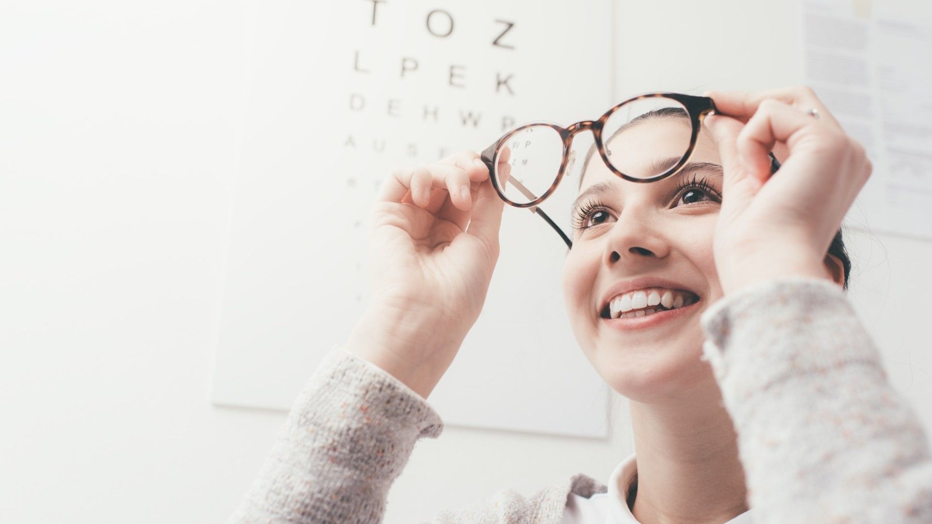 Eine Frau hält Ihre Brille vor das Gesicht und lächelt