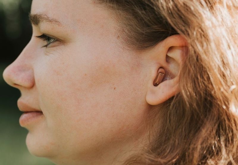 Eine junge Frau von der Seite fotografiert mit einem Hörgerät im Ohr